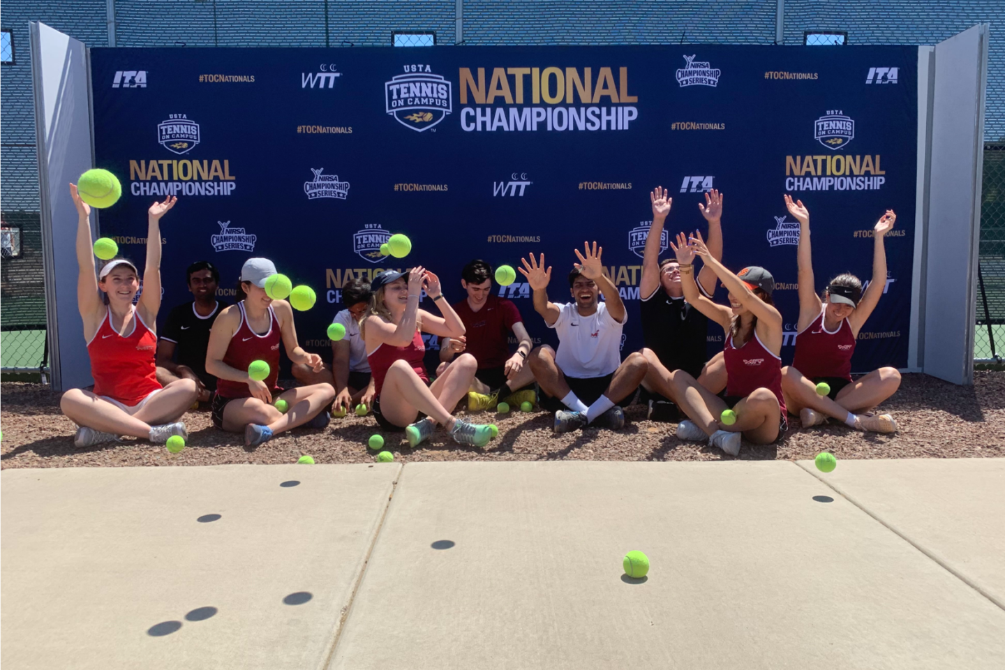 Team celebrating with arms in air. Tennis balls scattered